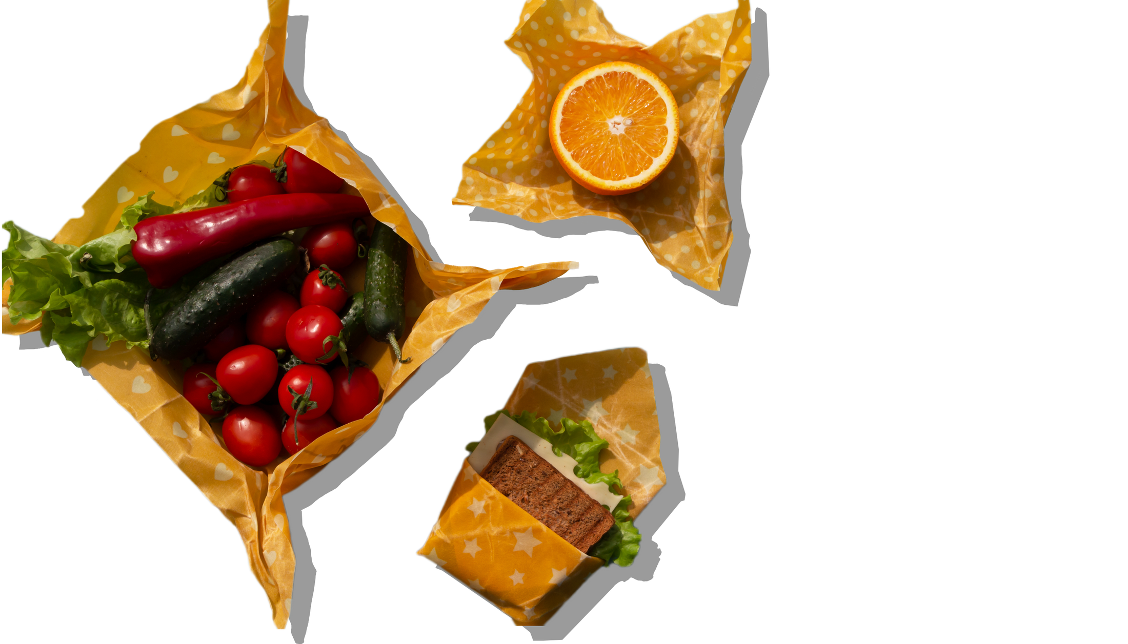 Beeswax wraps holding vegetables, an orange and a sandwich