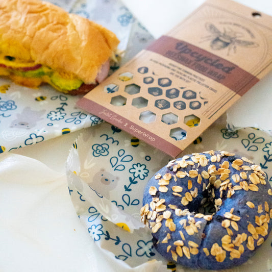A sandwich and a bagel wrapped in Superwrap’s upcycled beeswax wrap in the ‘Bear in the Garden’ design